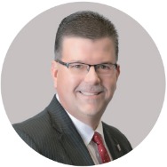 Man in a suit with a red tie smiling at the camera.