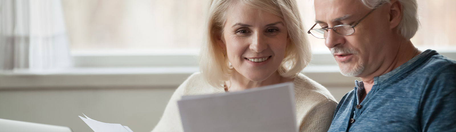 Mature couple smiles while reading paperwork together.
